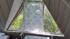 A triangular window with a leaf-patterned curtain, a glass table, and a bed with white bedding.