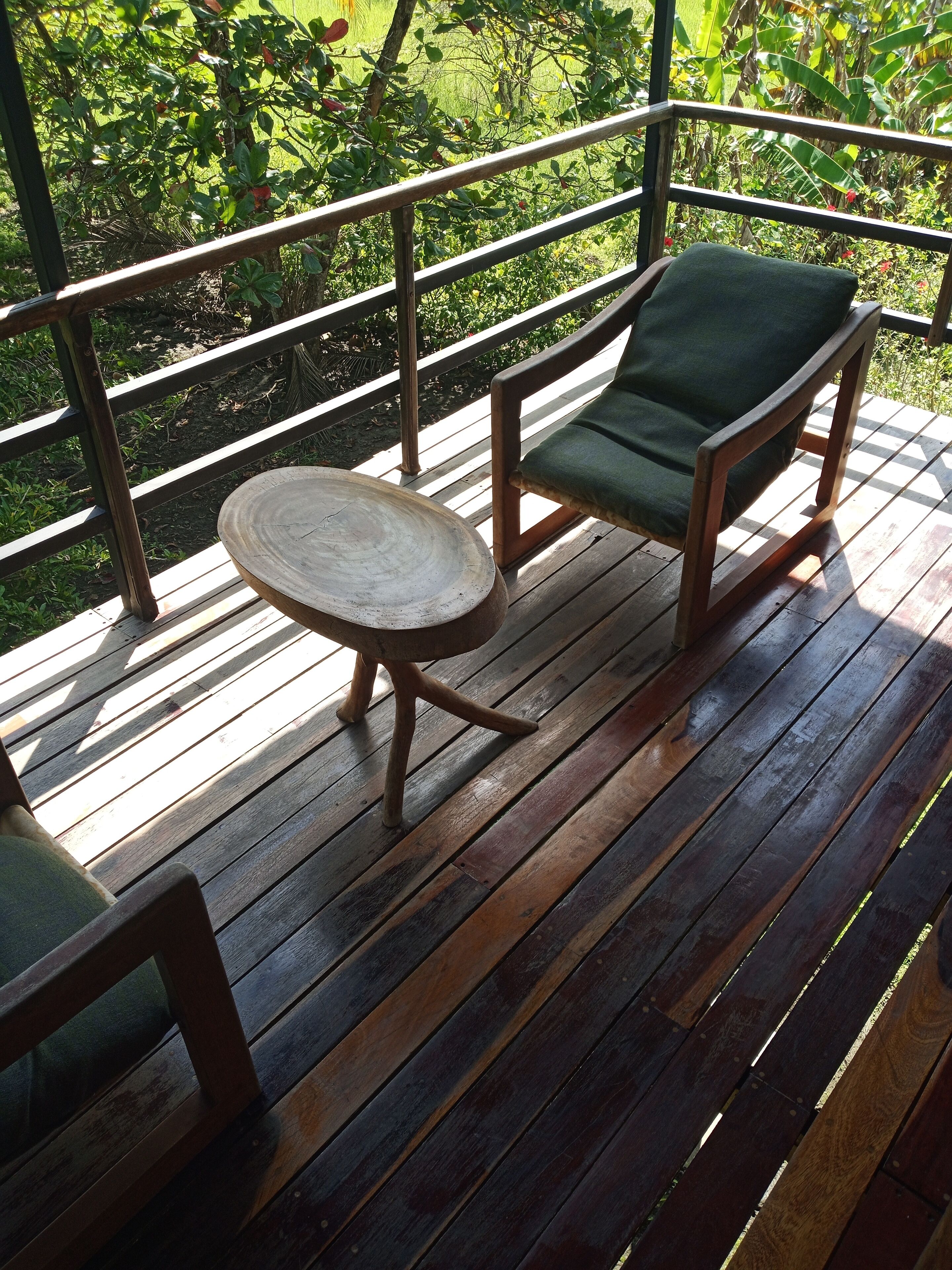 Una terraza de madera con una mesa redonda y una silla verde con cojín.