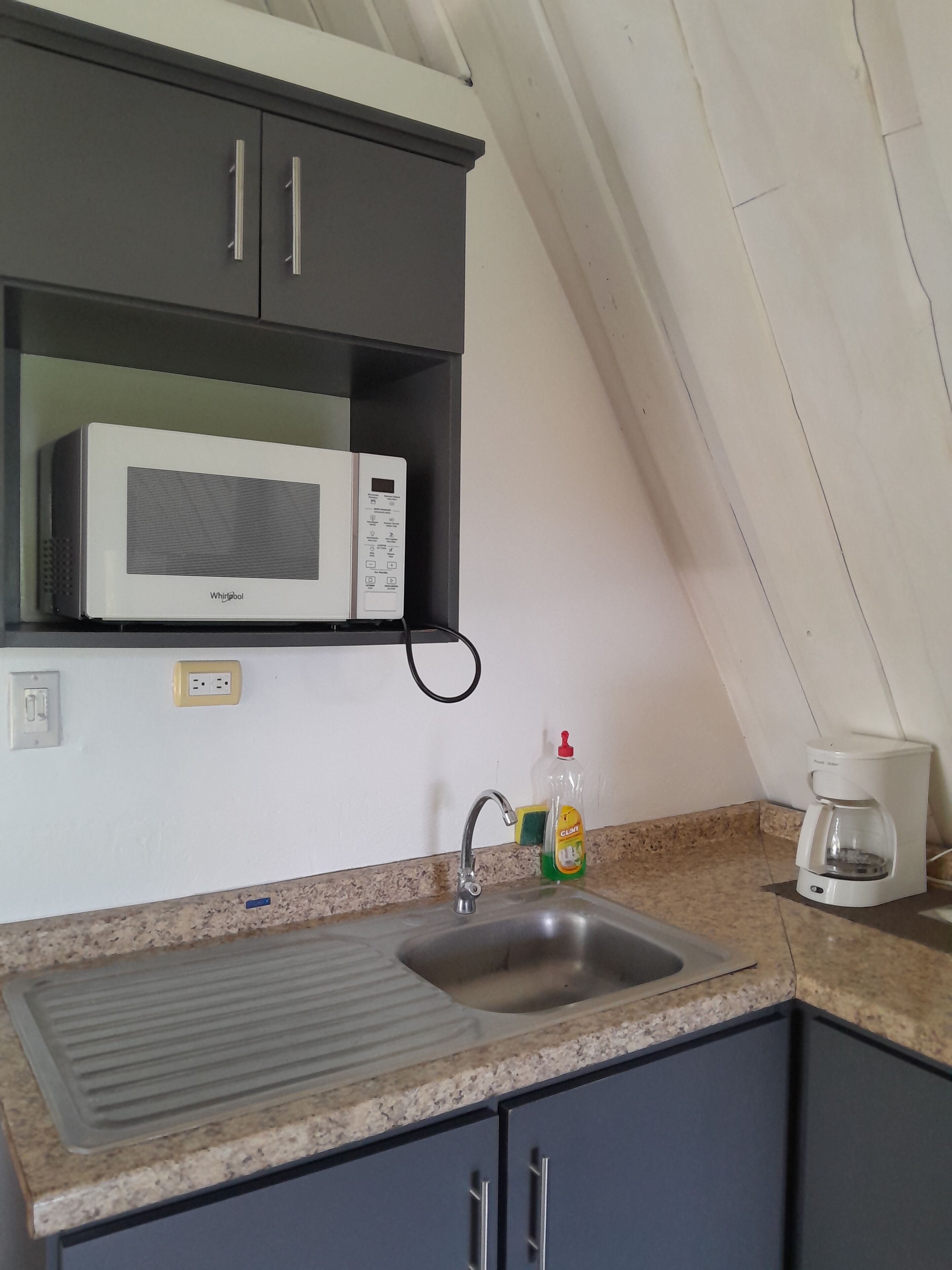 Eine Küche mit integriertem Mikrowellenherd, Spüle, Kaffeemaschine und einer Flasche Geschirrspülmittel.