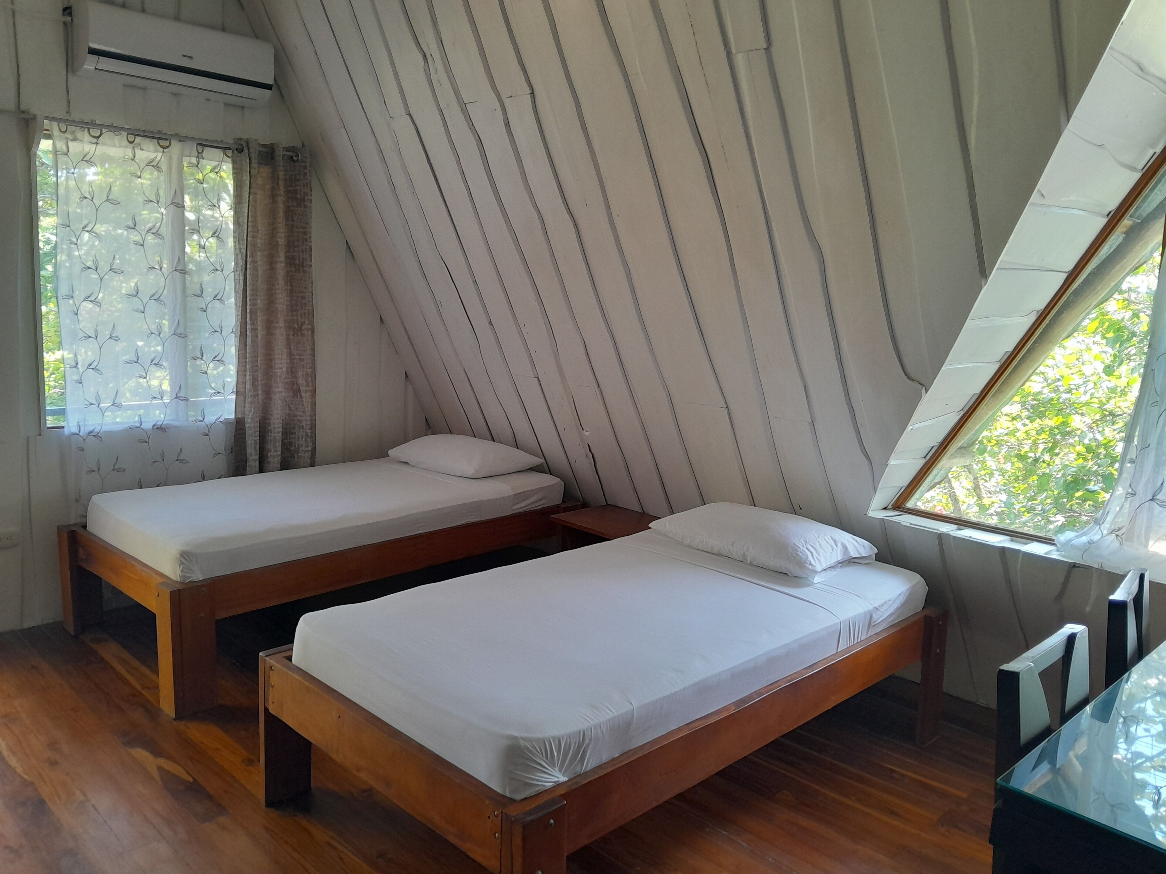 A room with two wooden beds, a wooden table, and a window with curtains.