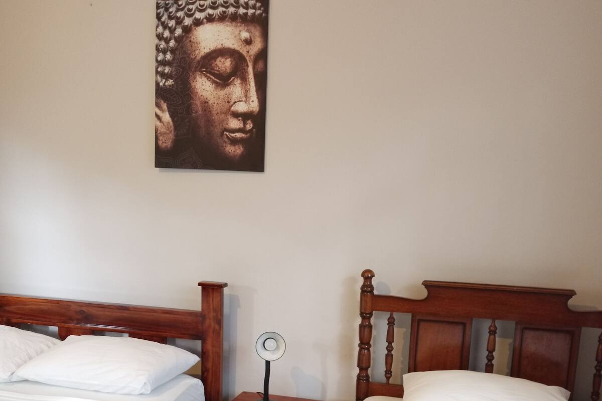 A bedroom with two wooden beds, a nightstand with a lamp, and a wall-mounted Buddha statue.