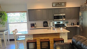 A modern kitchen with grey cabinets, a central island, a welcome sign, and a leather sofa.