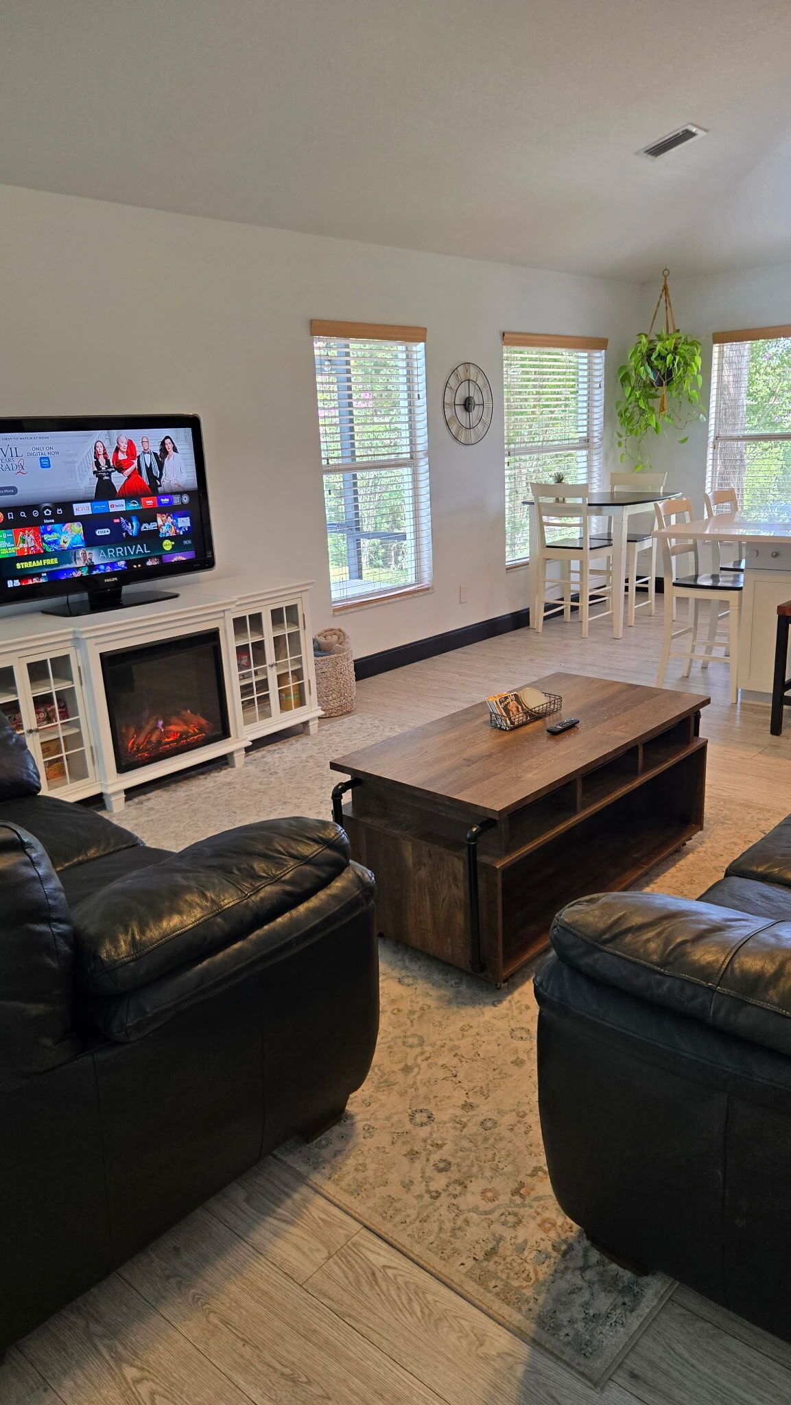 A living room with a TV, leather sofas, a wooden coffee table, a fireplace, and large windows.