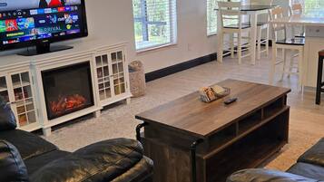 A living room with a TV, leather sofas, a wooden coffee table, a fireplace, and large windows.