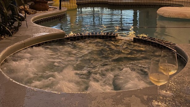 A hot tub with a pool, surrounded by rocks and a wooden deck.