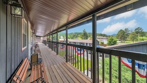 A covered porch with wooden flooring, metal railings, and a view of a parking lot and greenery. - Pine Top Balcony View (Hill City)