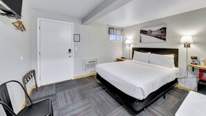 A hotel room with a large bed, a desk, a chair, a bedside table, a lamp, and a picture on the wall. - Pine Top Convenience (Hill City)