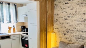 A modern living room with a grey sofa, a glass coffee table, and a kitchen area with white cabinets and a brick wall. - Extertal-Ferienpark - PREMIUM HOLIDAY HOUSE - Sauna, fireplace, hiking, relaxation #49 (Extertal)