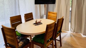 A dining area with a round table, six wooden chairs, and a flat-screen TV mounted on the wall. - Extertal-Ferienpark - PREMIUM HOLIDAY HOUSE - Sauna, fireplace, hiking, relaxation #49 (Extertal)