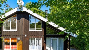 A two-story wooden house with a satellite dish, a garage, and a covered outdoor seating area. - Extertal-Ferienpark - PREMIUM HOLIDAY HOUSE - Sauna, fireplace, hiking, relaxation #49 (Extertal)