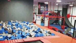 En gymnastiksal med en grop fylld med skumgummi, klätterställningar och en banderoll med texten ”NINJA WARRIOR”.