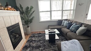 Un salon avec une cheminée, un canapé, une table basse et une grande fenêtre.