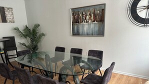 Une salle à manger moderne avec une table en verre entourée de six chaises, un grand tableau au mur et une plante en pot.