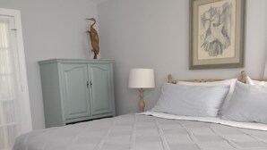 Una cama bien hecha con edredón blanco, un armario azul claro, una mesita de noche de madera y un cuadro enmarcado en la pared.