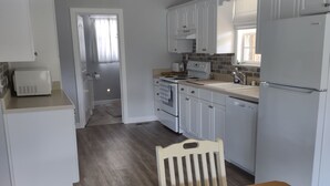 Cocina compacta con armarios blancos, una mesa de madera con un tablero de ajedrez y vista hacia la habitación contigua.