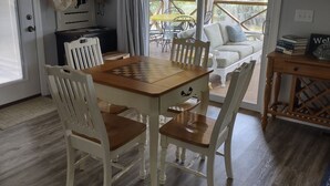Un comedor con una mesa de madera y sillas blancas, una cocina con estufa y alacenas, y un balcón con mobiliario exterior.