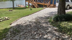 Una cabaña junto al lago con un muelle, un balcón y un camino de grava que lleva a la cabaña.