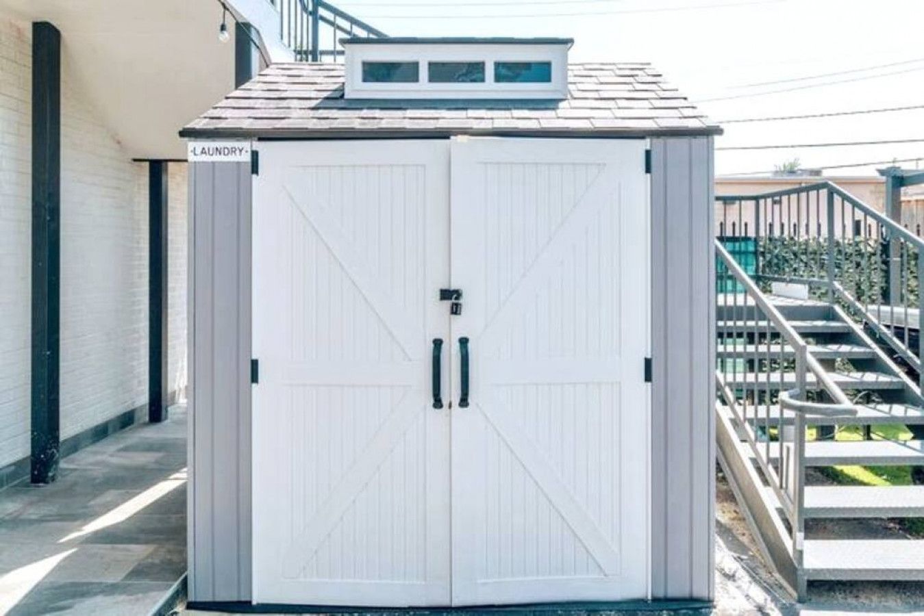 A white, double-door laundry facility with a small window on the roof, located next to a staircase.