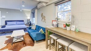 A modern hotel room with a bed, blue sofa, wooden dining table, and a cowhide rug.