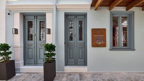 Entrada de un hotel con dos puertas dobles grises, un letrero de madera y una ventana con vidrio esmerilado.