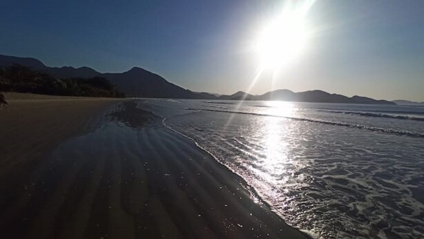 A beach with a clear sky and mountains in the background.
