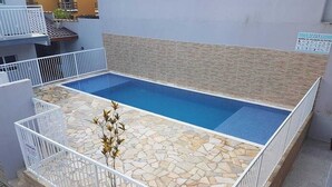 A rectangular pool with a stone tile deck, surrounded by white railings and a potted plant.