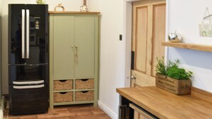 Cucina con frigorifero nero, mobili verdi, pavimento in legno e piano di lavoro in legno con una pianta.