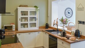 Una cucina compatta con mobili bianchi, un piano di lavoro in legno, un forno a microonde integrato, una macchina da caffè e una sveglia a muro.