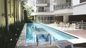 A swimming pool with a clear lane, surrounded by lounge chairs and a wooden deck. - Studio ao lado do Allianz Parque (São Paulo)