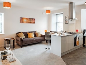 Una cocina moderna con una isla central, un sofá con cojines y una zona de comedor con mesa y sillas.