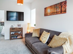 Una sala de estar con un sofá gris, un televisor de pantalla plana, un mueble de madera y un cuadro en la pared.