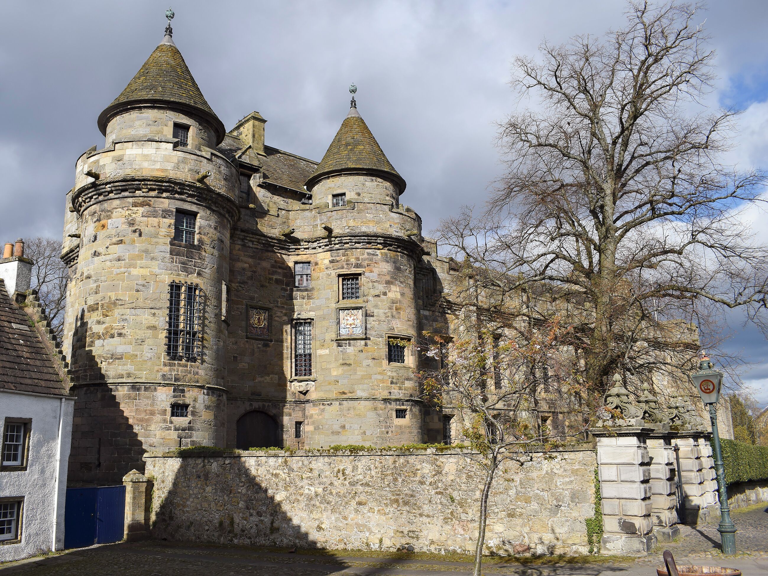 A historic stone castle with multiple towers and a large tree in front.