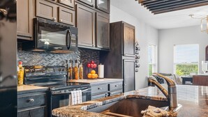 A modern kitchen with dark cabinetry, a granite countertop, a stainless steel sink, and a built-in microwave. - Newly Redesigned Lakefront Condo with Dock near Downtown Fun! (Hot Springs)