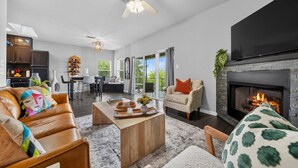 A modern living room with a fireplace, leather sofa, and a dining area with a chandelier. - Newly Redesigned Lakefront Condo with Dock near Downtown Fun! (Hot Springs)