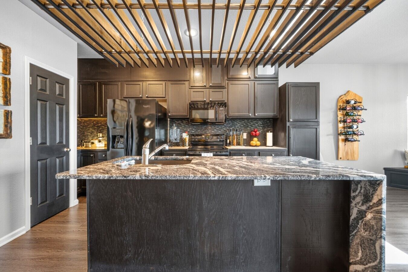 Une cuisine moderne avec des meubles de couleur sombre, un grand îlot central en granit et un design de plafond original.