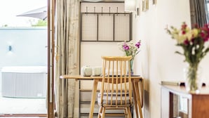 Ein Zimmer mit Holzstuhl, kleinem Tisch, Blumen in einer Vase, Handtuchhalter und einem Fenster mit Aussicht.