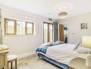 Ein Schlafzimmer mit Bett, Nachttisch, Lampe und Blick durch ein Fenster nach draußen.