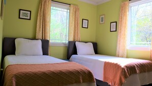 Une chambre avec deux lits, une fenêtre avec des rideaux et des tableaux encadrés au mur.