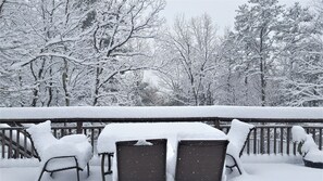 Une terrasse enneigée, avec une table et des chaises, entourée d’arbres.