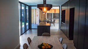 A modern kitchen with a central island, a dining area with a wooden table, and a large window providing natural light. - Casa Familiar com Piscina (Ponta Delgada)