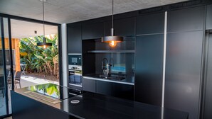 A modern kitchen with a black countertop, stainless steel appliances, and pendant lighting. - Casa Familiar com Piscina (Ponta Delgada)