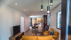 A modern living room with a large sofa, a flat-screen TV, and a dining area with a table and chairs. - Casa Familiar com Piscina (Ponta Delgada)
