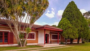 A two-story house with a red roof and brick walls, surrounded by a well-maintained lawn and large trees. - Sítio King - Bragança Paulista (Piracaia)