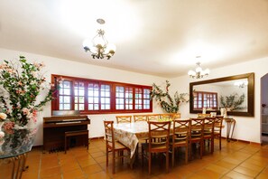 A dining area with a piano, wooden chairs, a table with a floral tablecloth, and a large mirror on the wall. - Sítio King - Bragança Paulista (Piracaia)