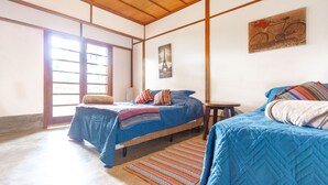 A room with two beds, a wooden ceiling, a large window, and a painting of a bicycle. - Sítio King - Bragança Paulista (Piracaia)