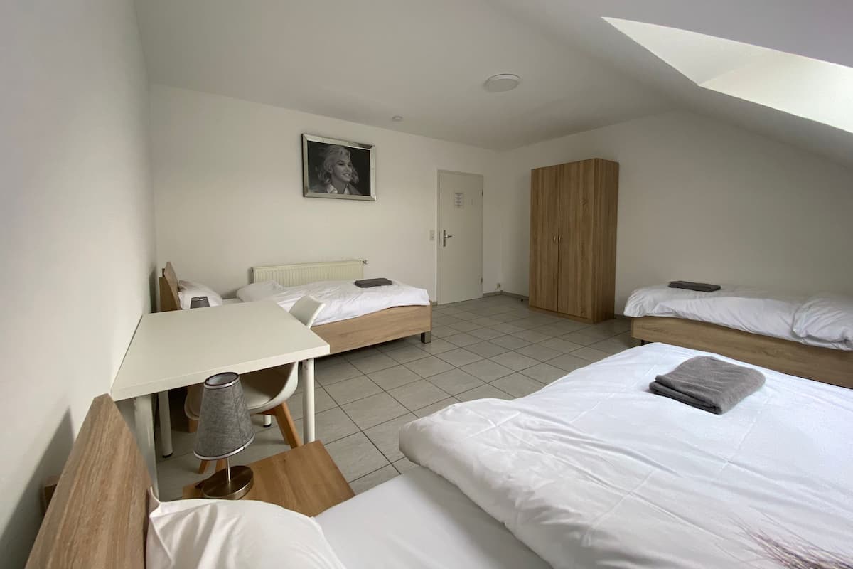 A dorm-style room with two single beds, a desk, a chair, a wardrobe, and a framed picture on the wall.