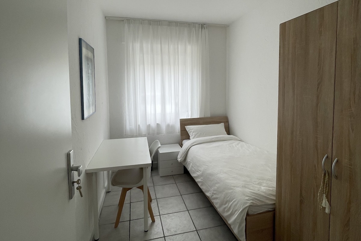 A small, clean room with a bed, a desk, and a wardrobe.
