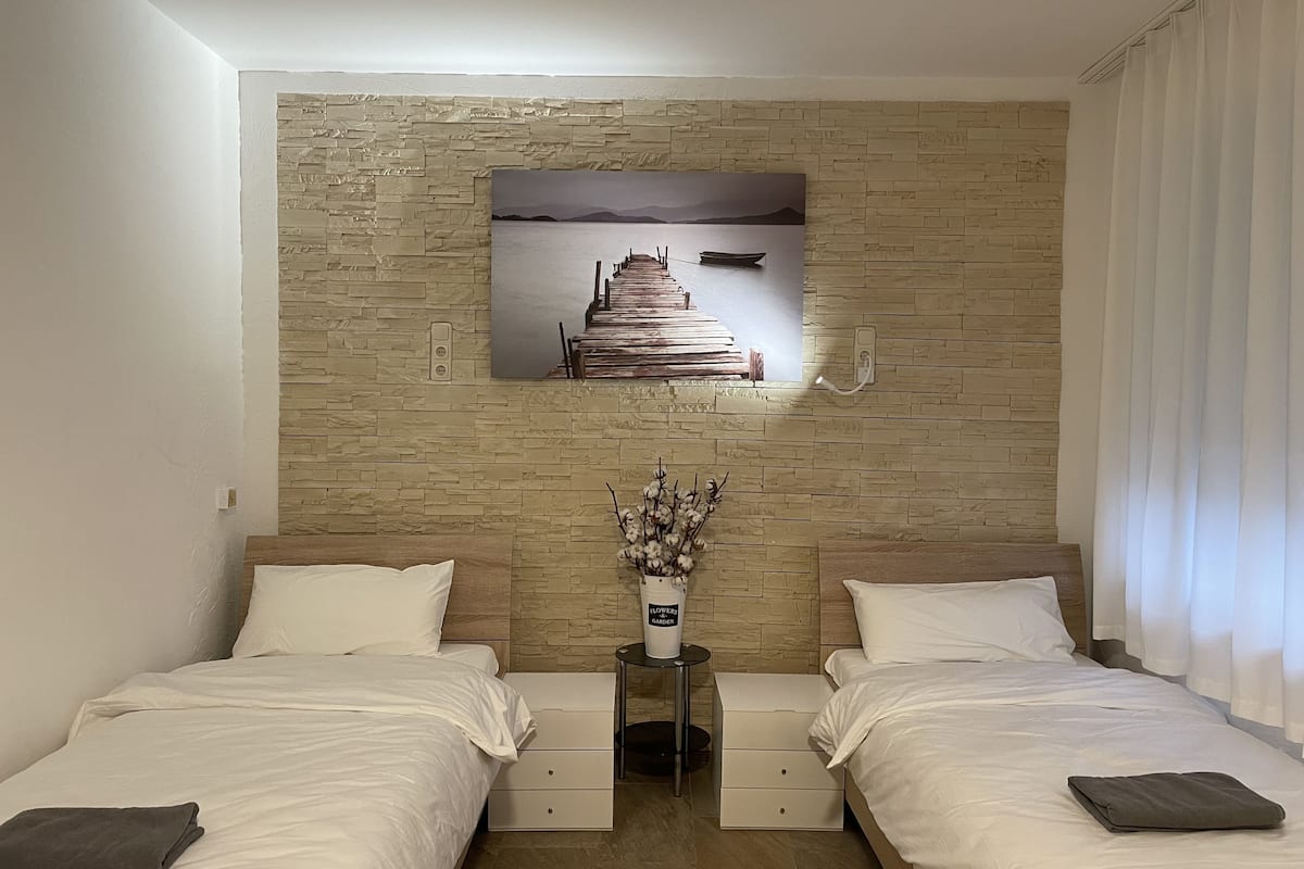 A hotel room with two beds, a stone wall, a painting of a dock, and a vase with flowers.