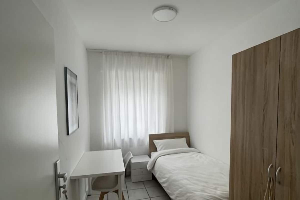 A small, clean room with a bed, a desk, and a wardrobe.