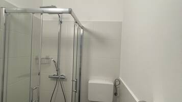 A bathroom with a glass-enclosed shower, a toilet, and a sink.